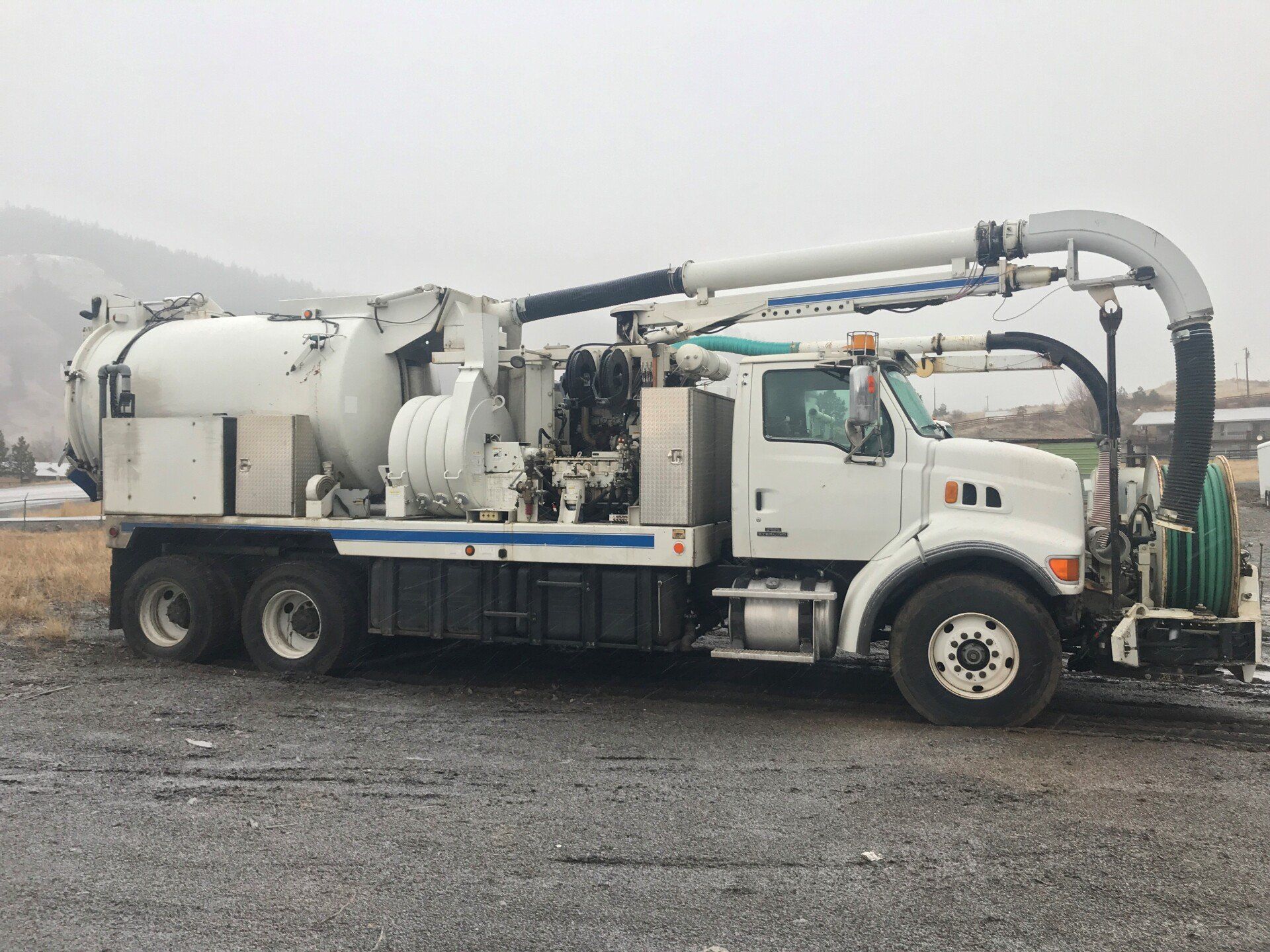 A white vacuum truck is parked in a gravel lot.