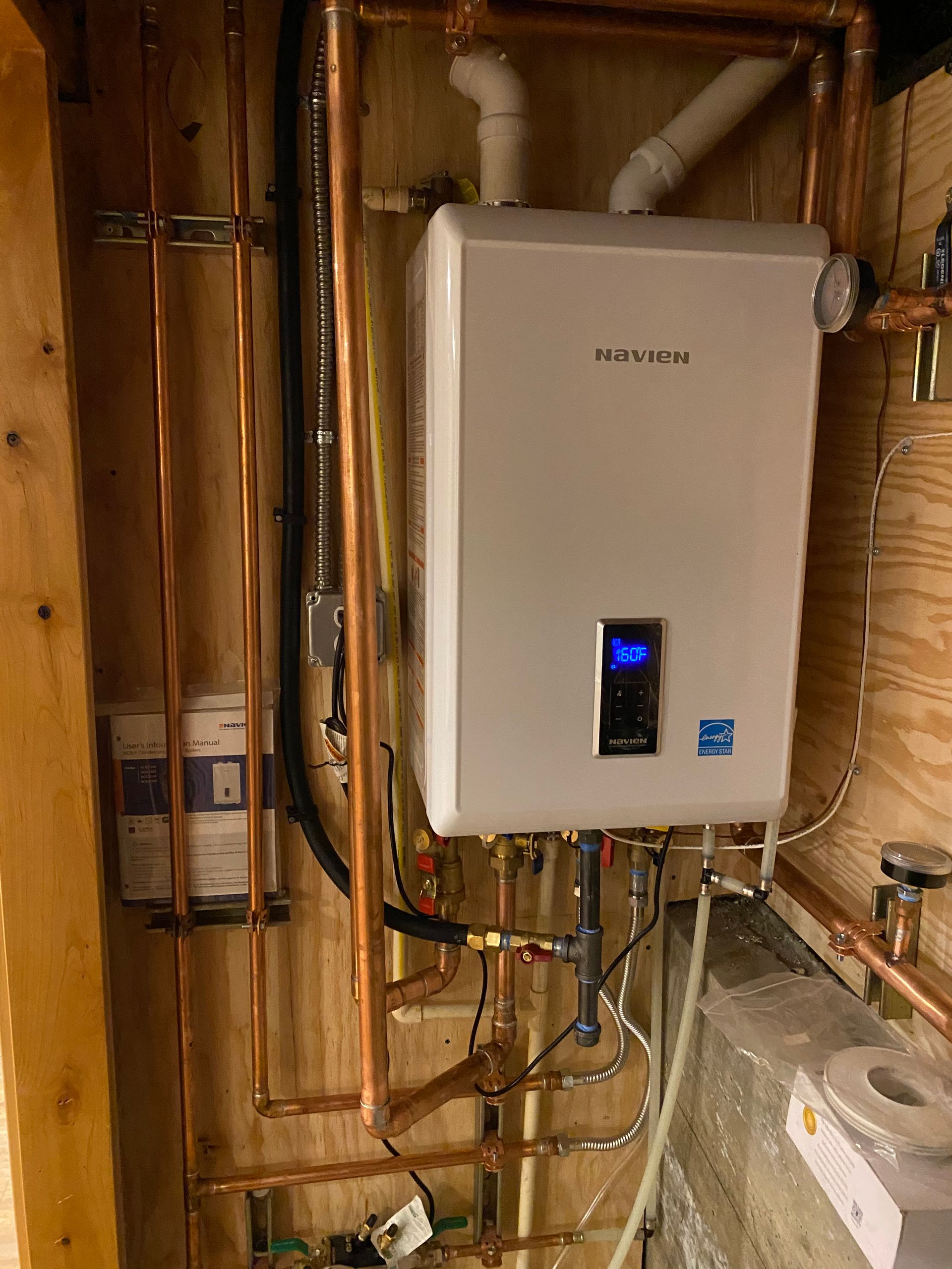 A white water heater is hanging on a wall next to copper pipes.