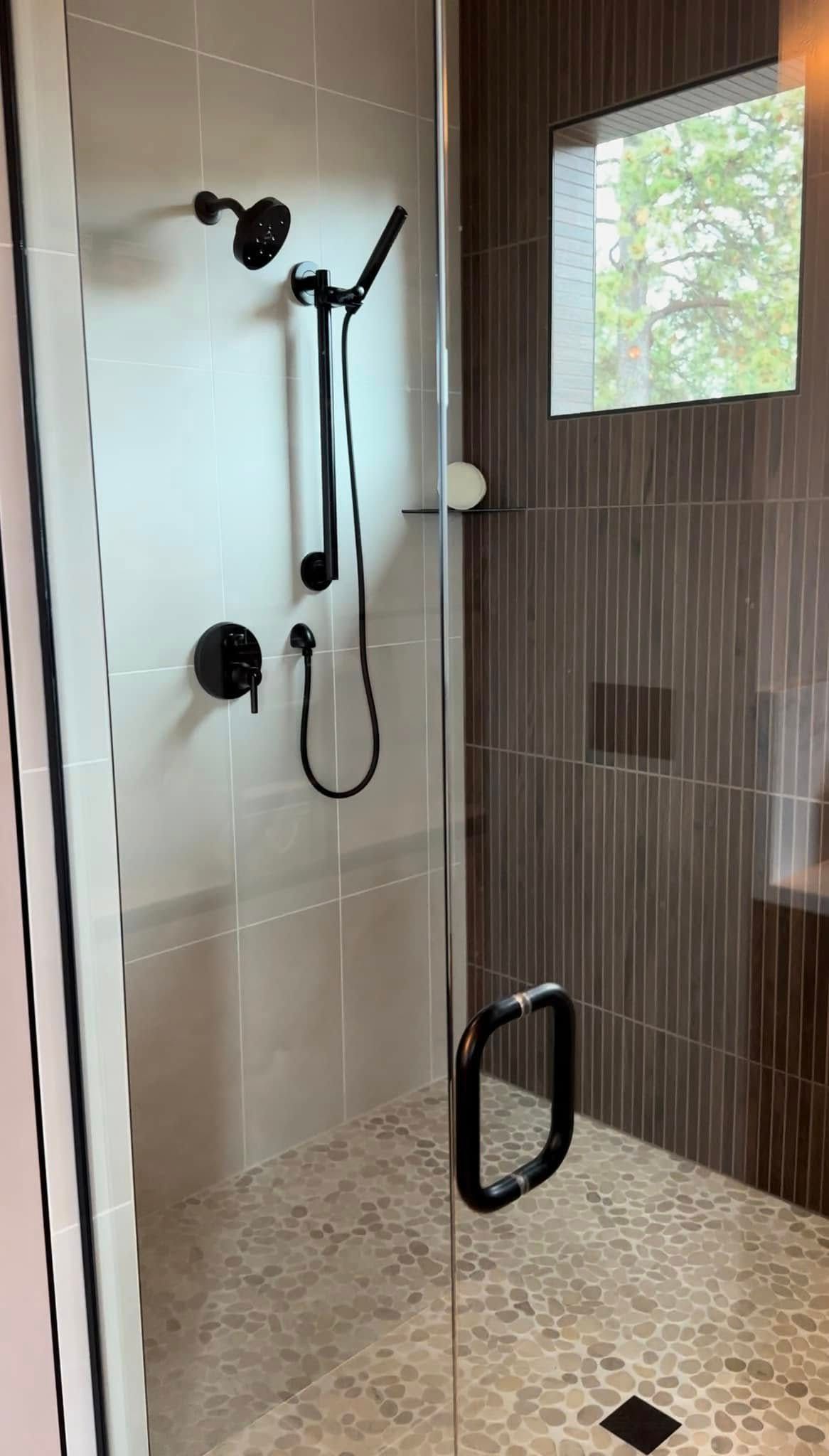 A walk in shower with a glass door and a window