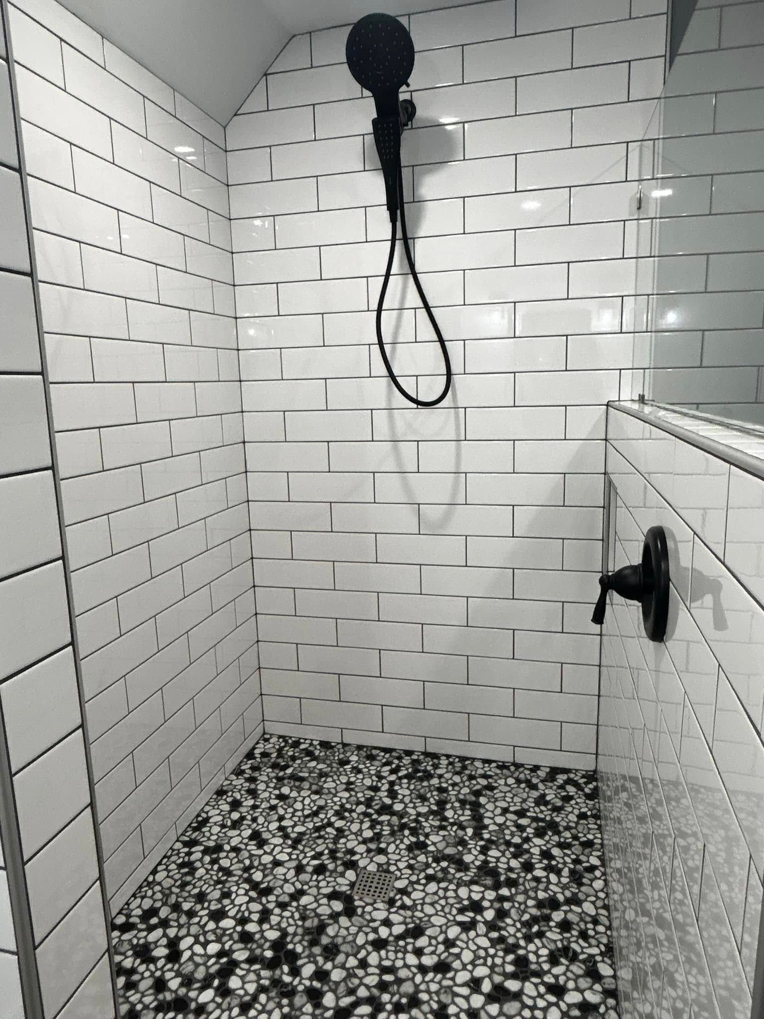 A shower with black and white tiles and a black shower head