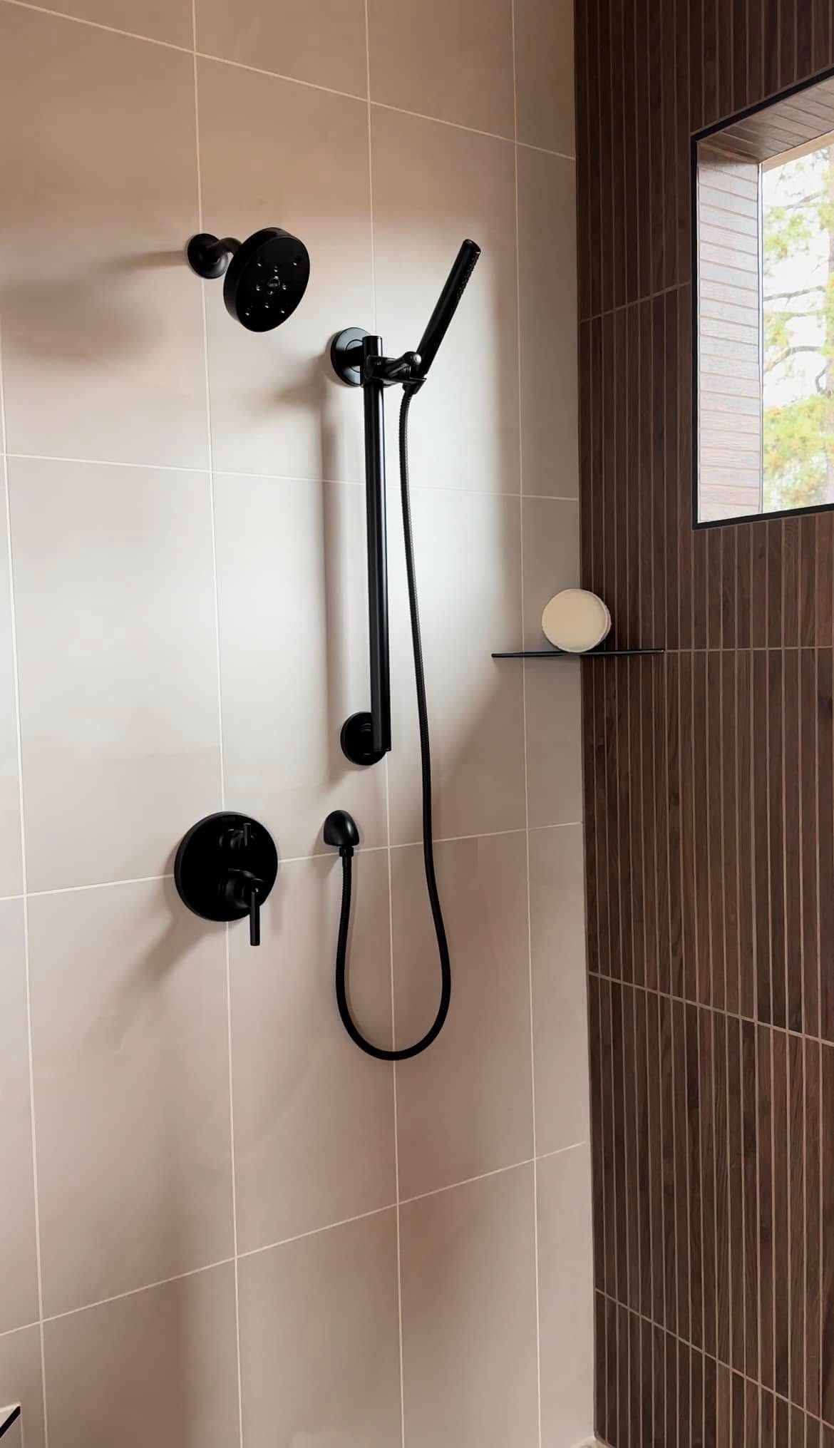 A shower with a black shower head and a window