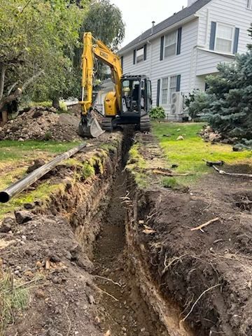 A yellow excavator is digging a trench in front of a house.
