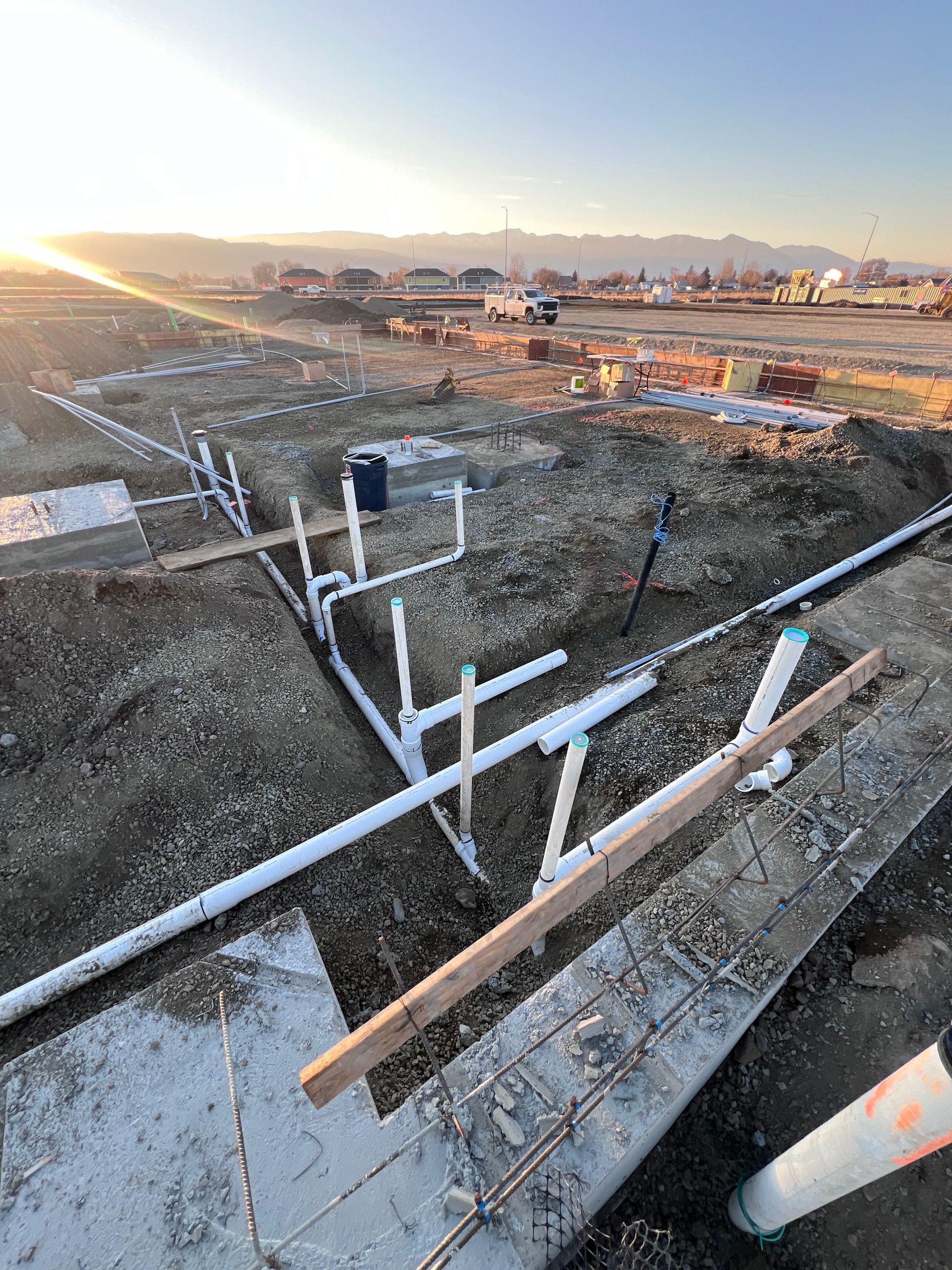 A bunch of pipes are laying in the dirt on a construction site.