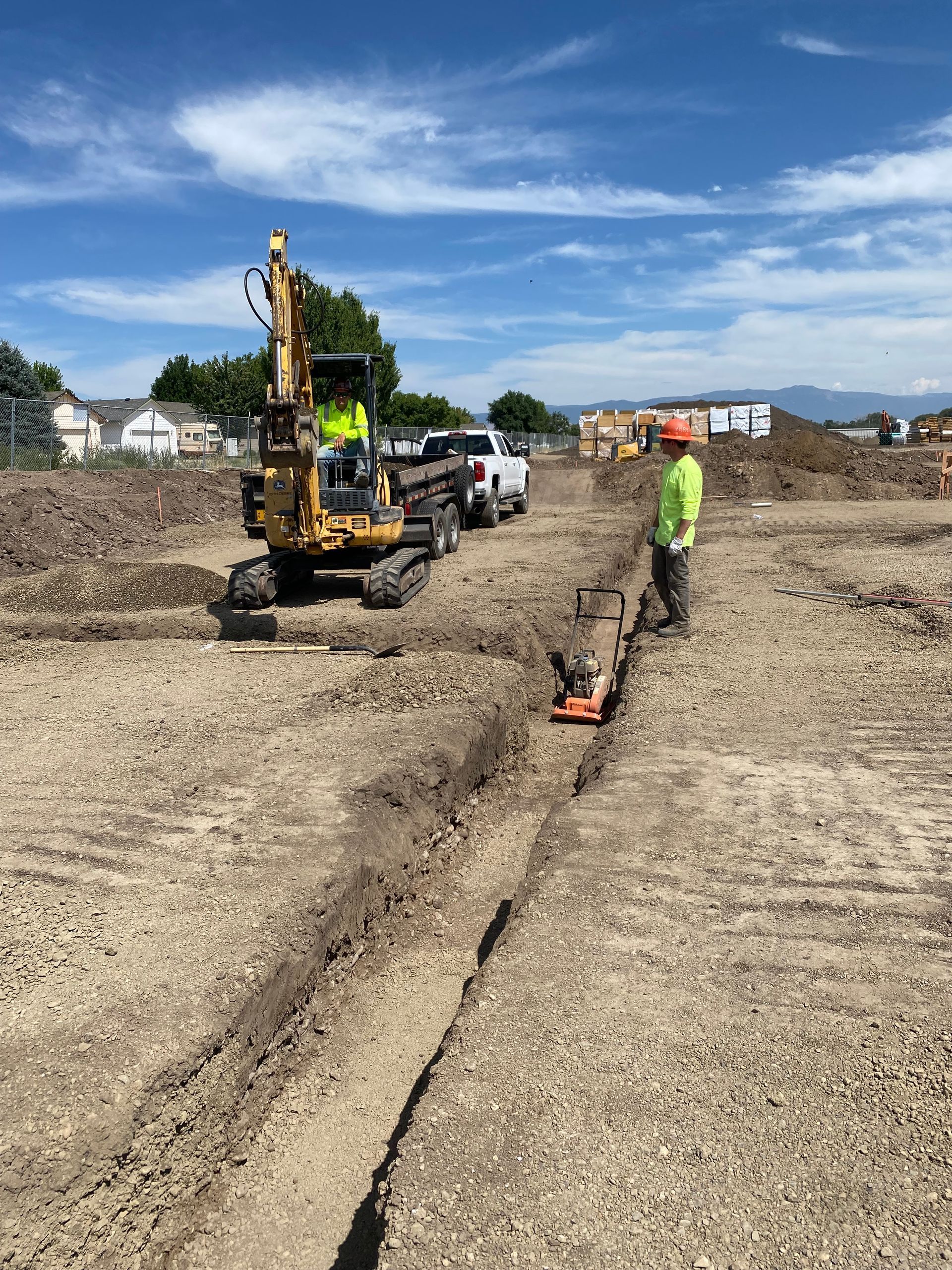 A construction worker is standing next to a yellow excavator.