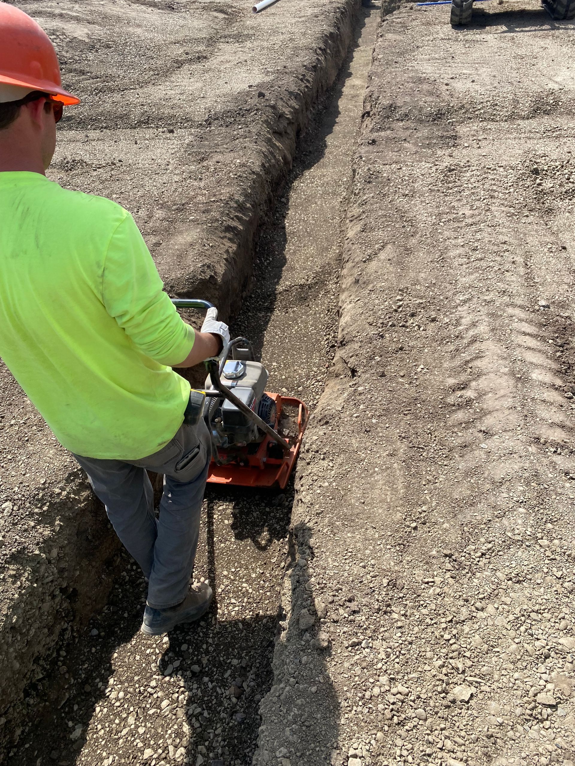 A construction worker is using a machine to dig a trench in the dirt.