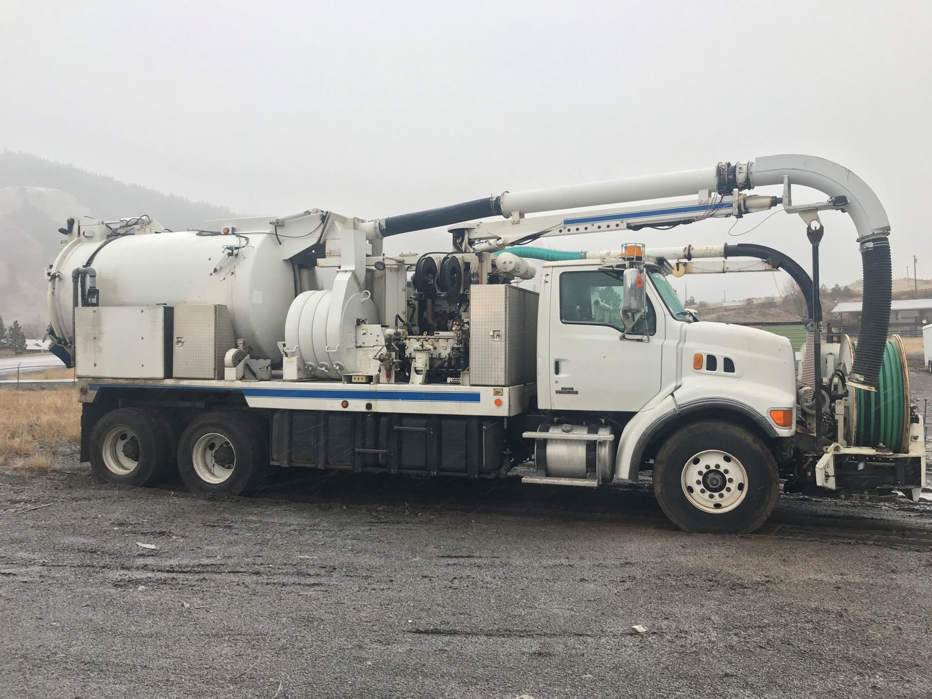 A white vacuum truck is parked in a gravel lot.