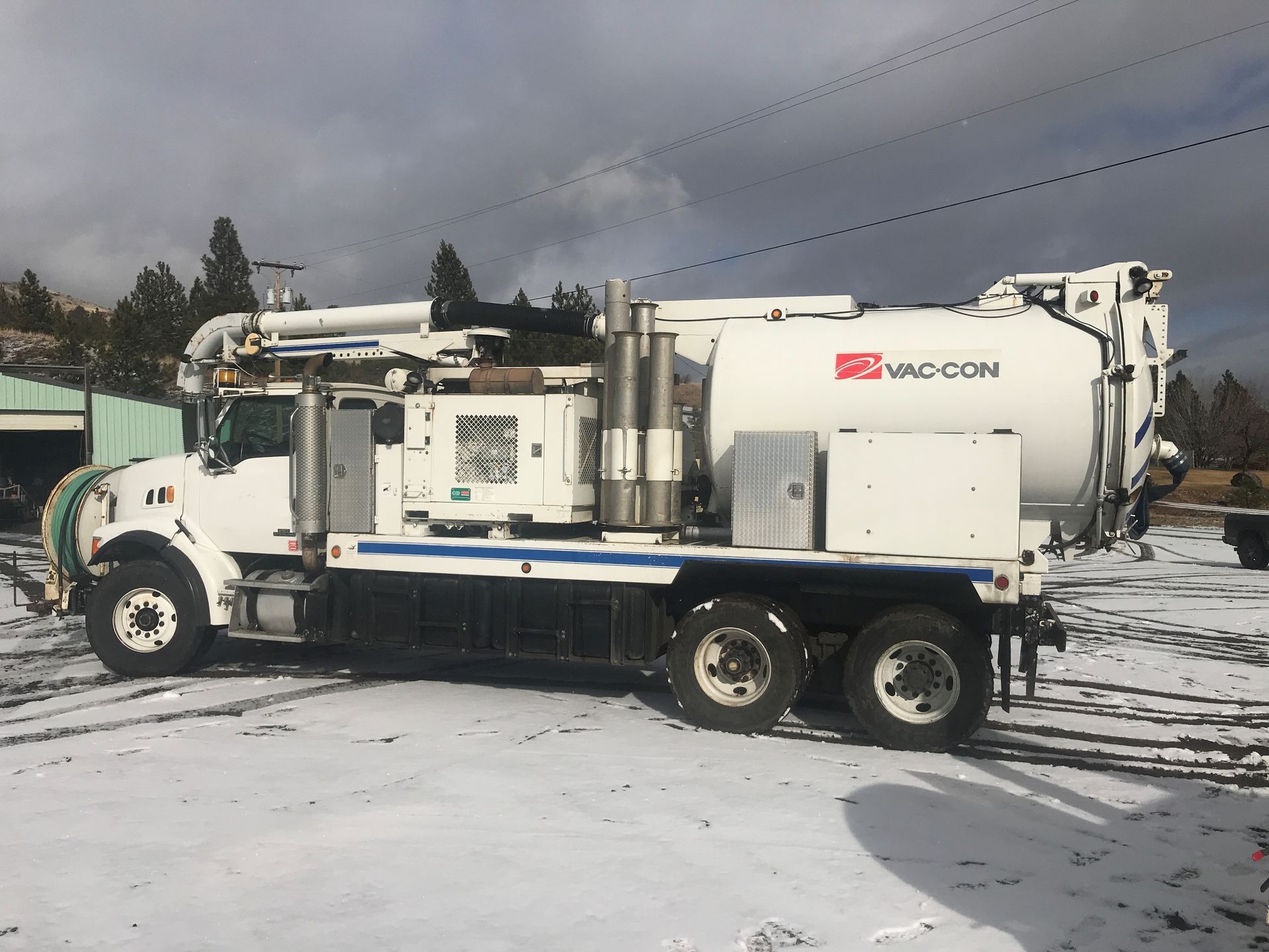 A white and blue vacuum truck is parked in a snowy lot.