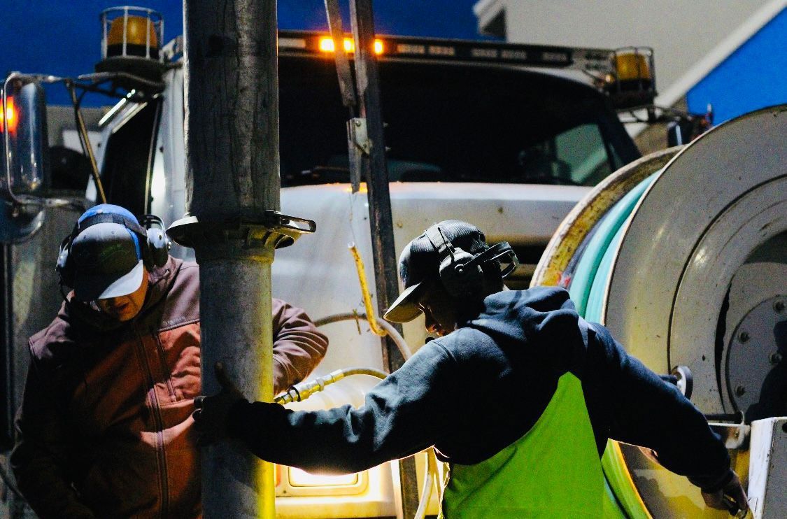A man in a yellow vest is working on a pipe next to a truck.