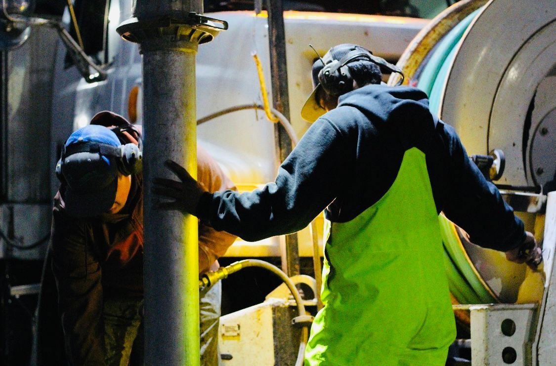 Two men are working on a pipe in front of a truck.