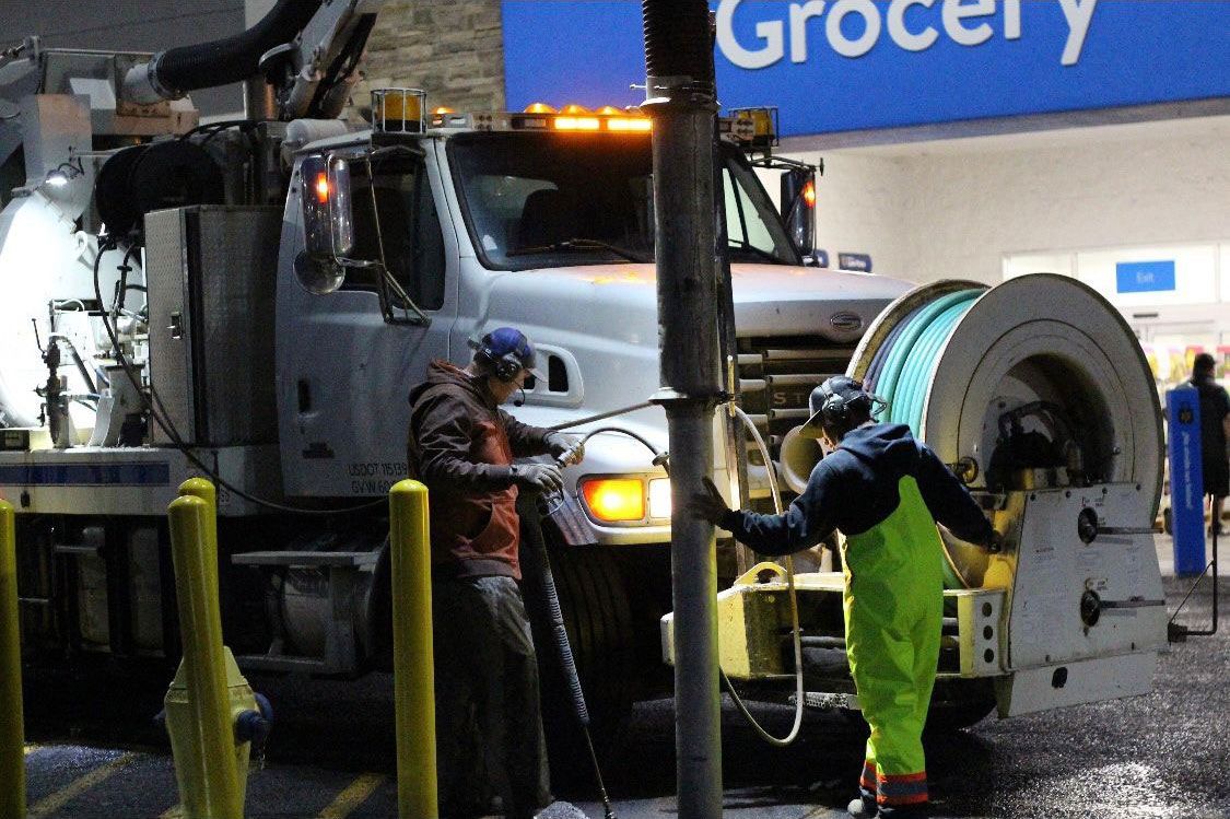 Two men are working on a drain in front of a grocery store.
