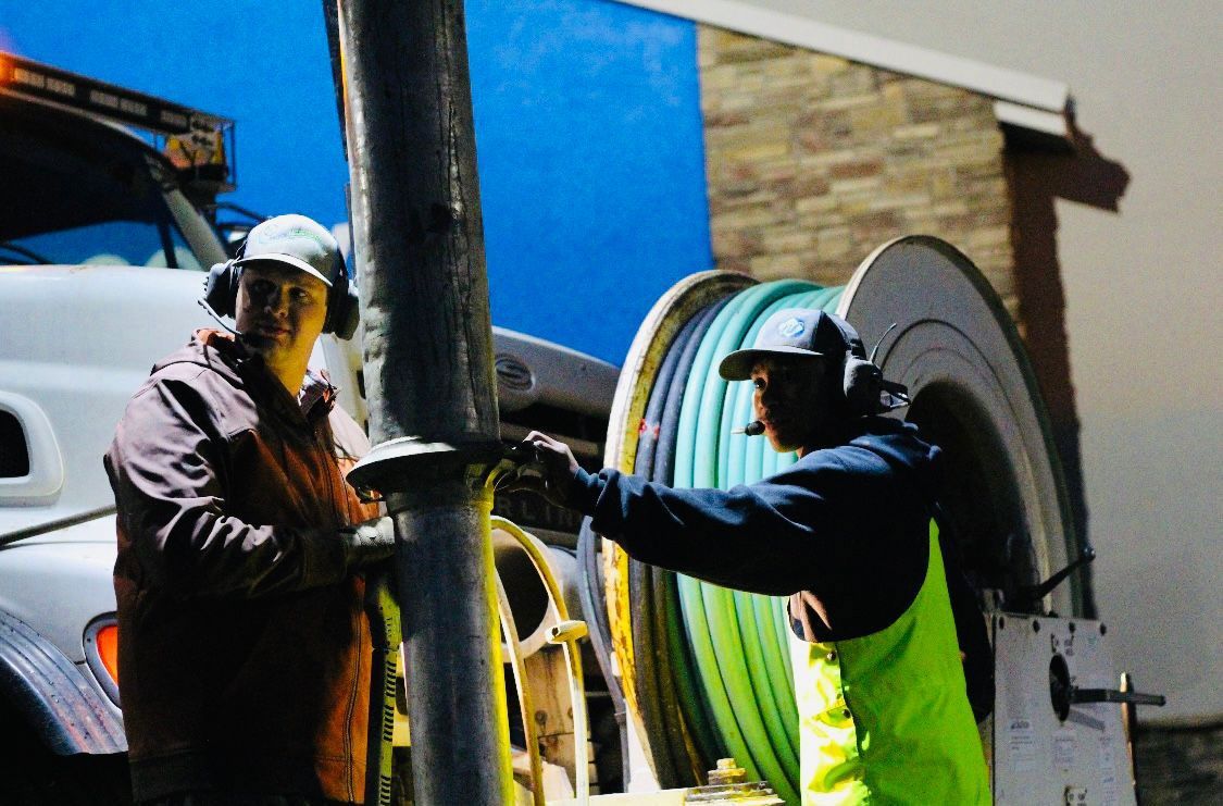 Two men are working on a pipe in front of a truck.