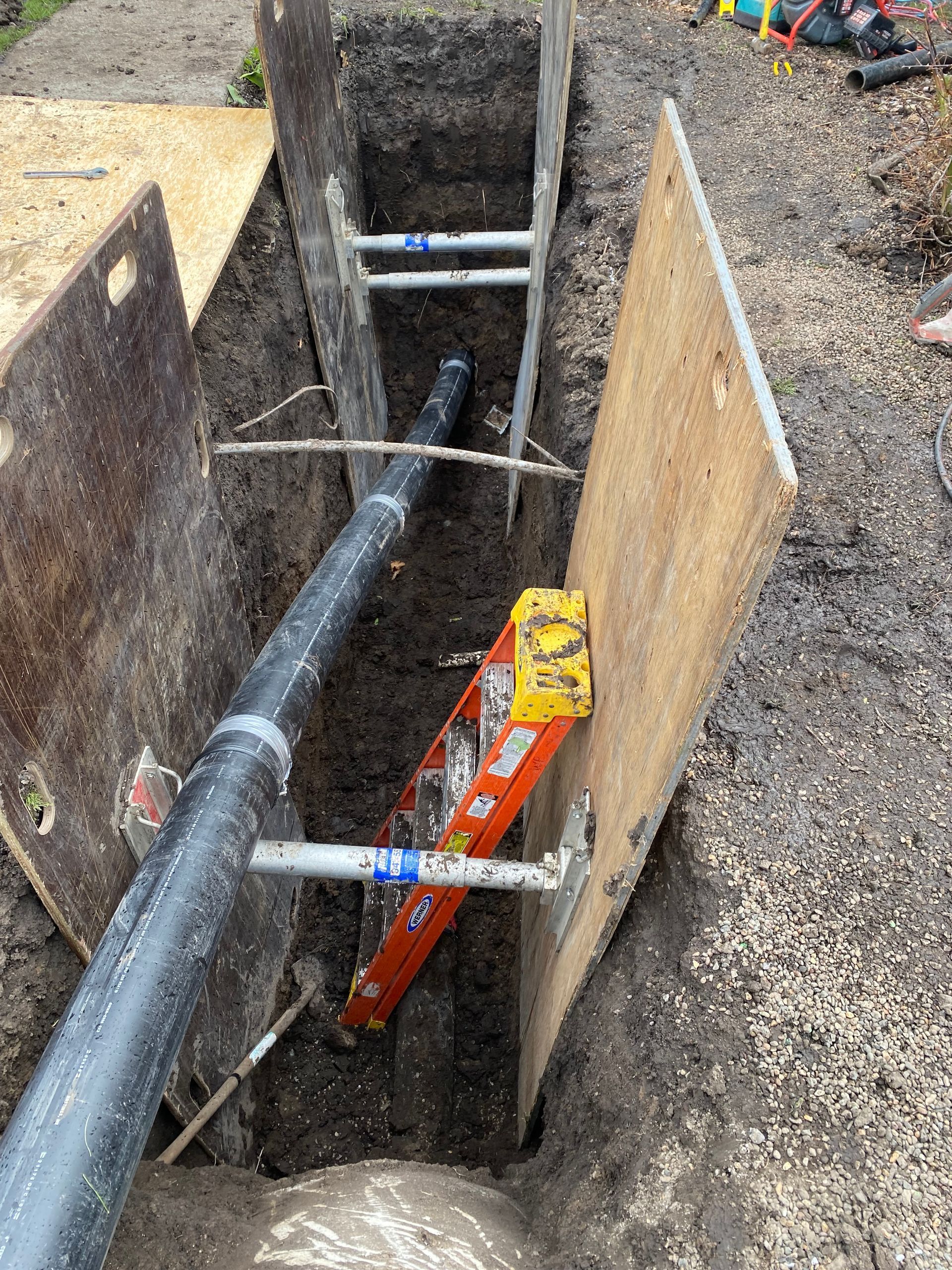 A ladder is sitting in the dirt next to a pipe.