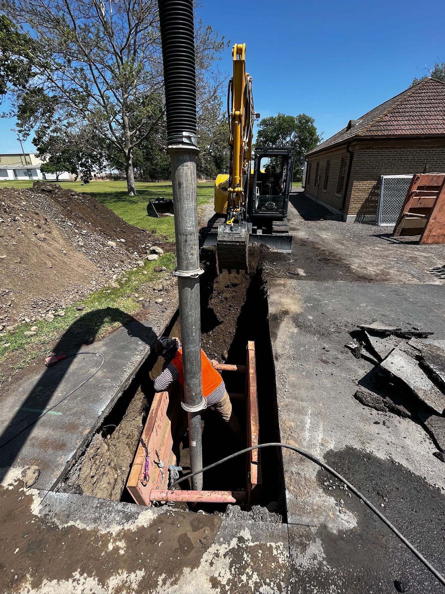 A yellow excavator is digging a hole in the ground in front of a house