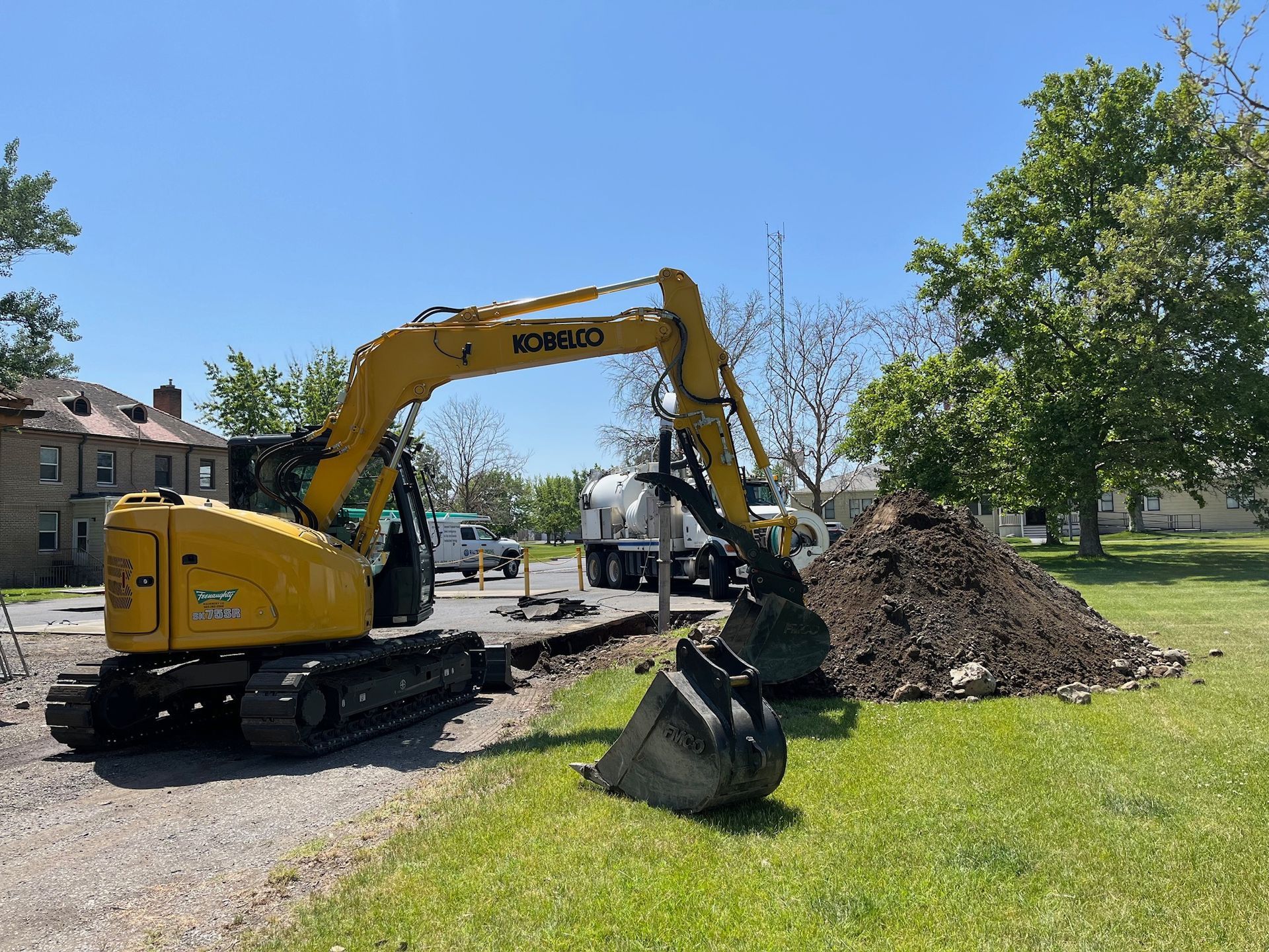 A yellow excavator is digging a hole in the grass