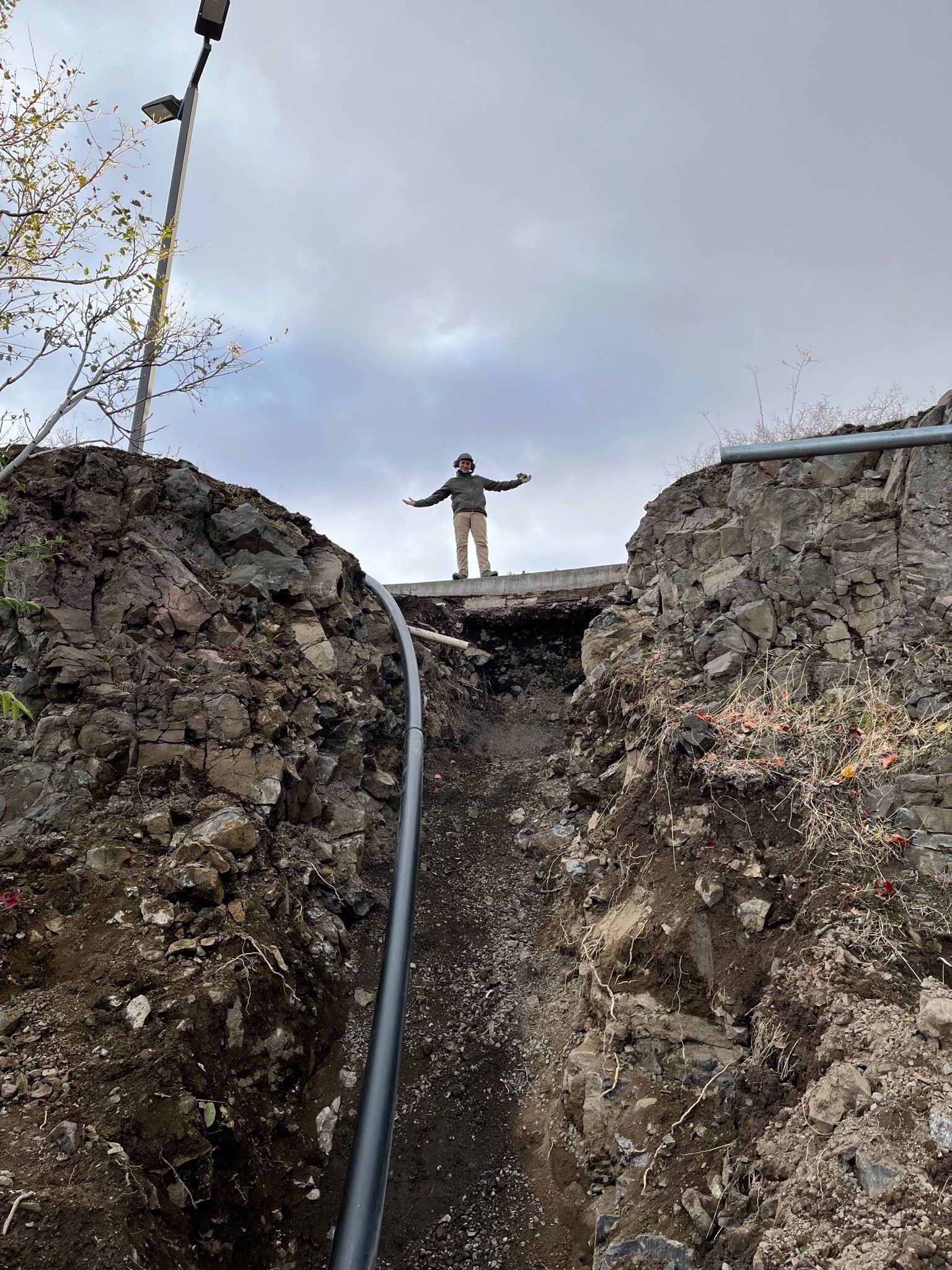 A man is standing on top of a pile of dirt next to a pipe