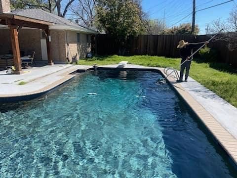 Person cleaning a turquoise pool with a long-handled tool; house and yard in the background.