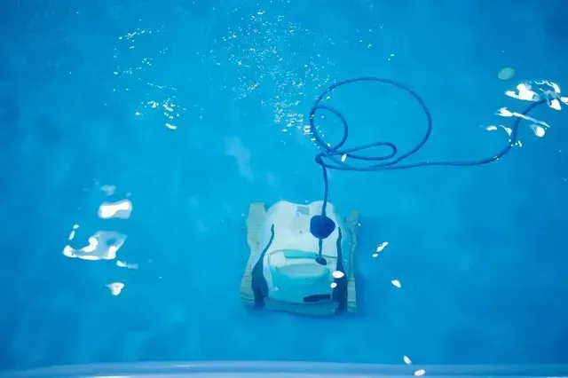 Underwater view of a robotic pool cleaner in a blue pool, with a coiled blue cable and bubbles.