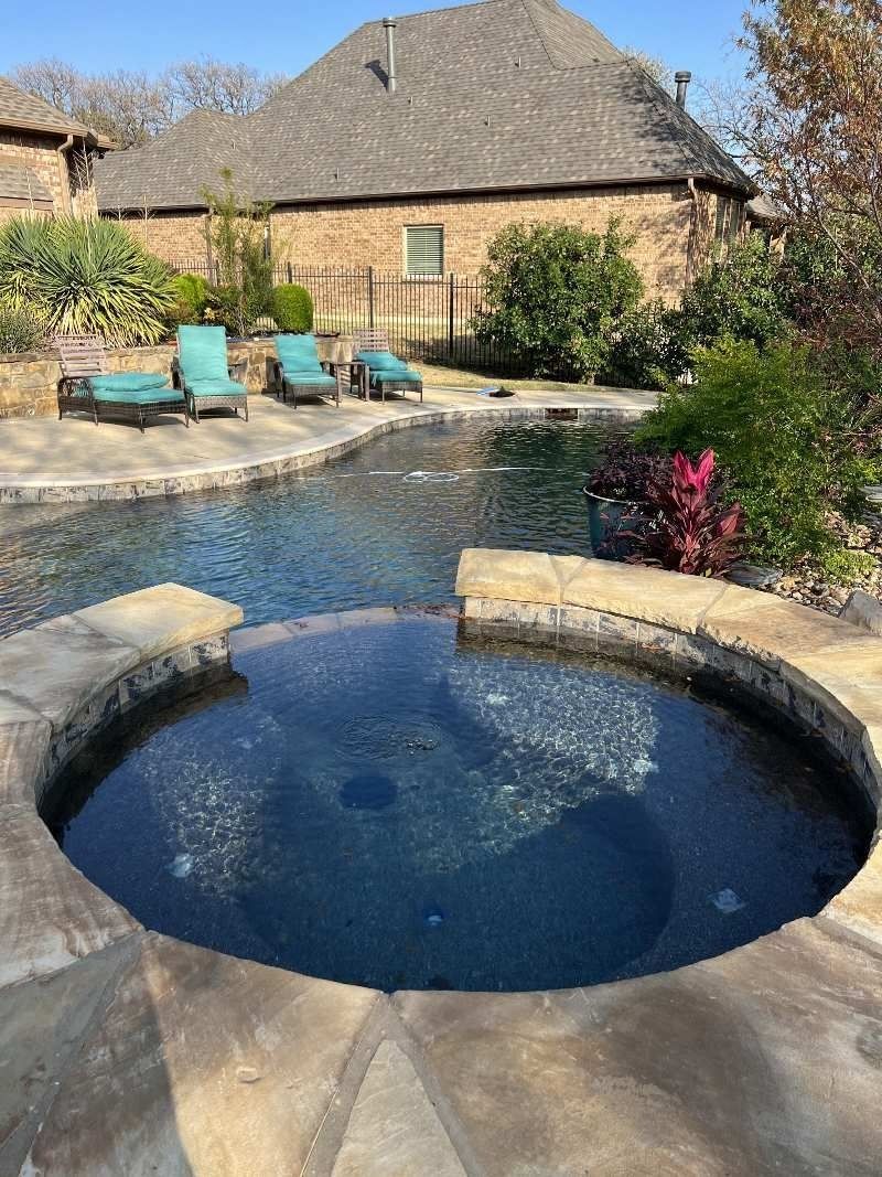 Swimming pool with spa, lounge chairs, and landscaping in front of a brick house.