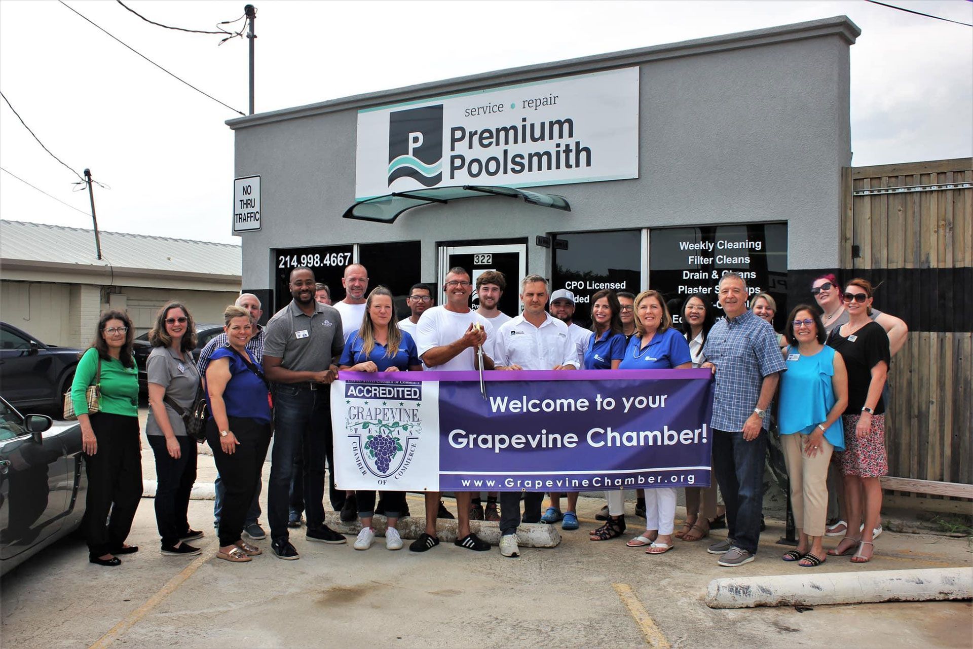 Group of people holding a banner in front of a store with a sign that reads &ldquo;Premium Poolsmith&rdquo;.