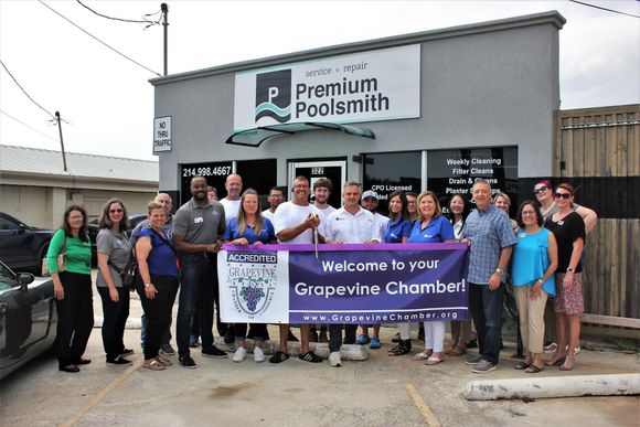 Group of people holding a banner in front of a store with a sign that reads “Premium Poolsmith”.