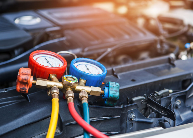 Red and blue gauges with hoses connected to a car’s open engine bay for air-conditioning service