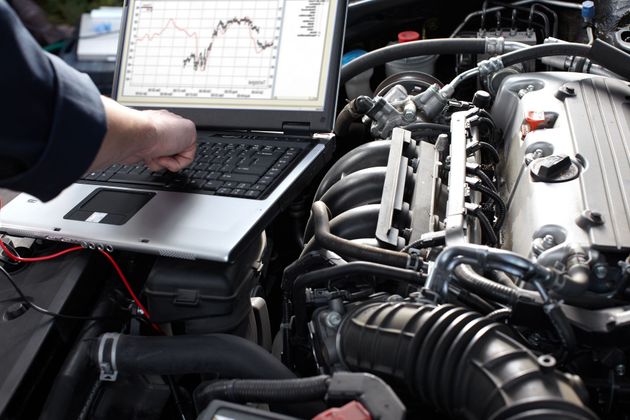 Mechanic using a laptop to diagnose a car engine in an open hood bay