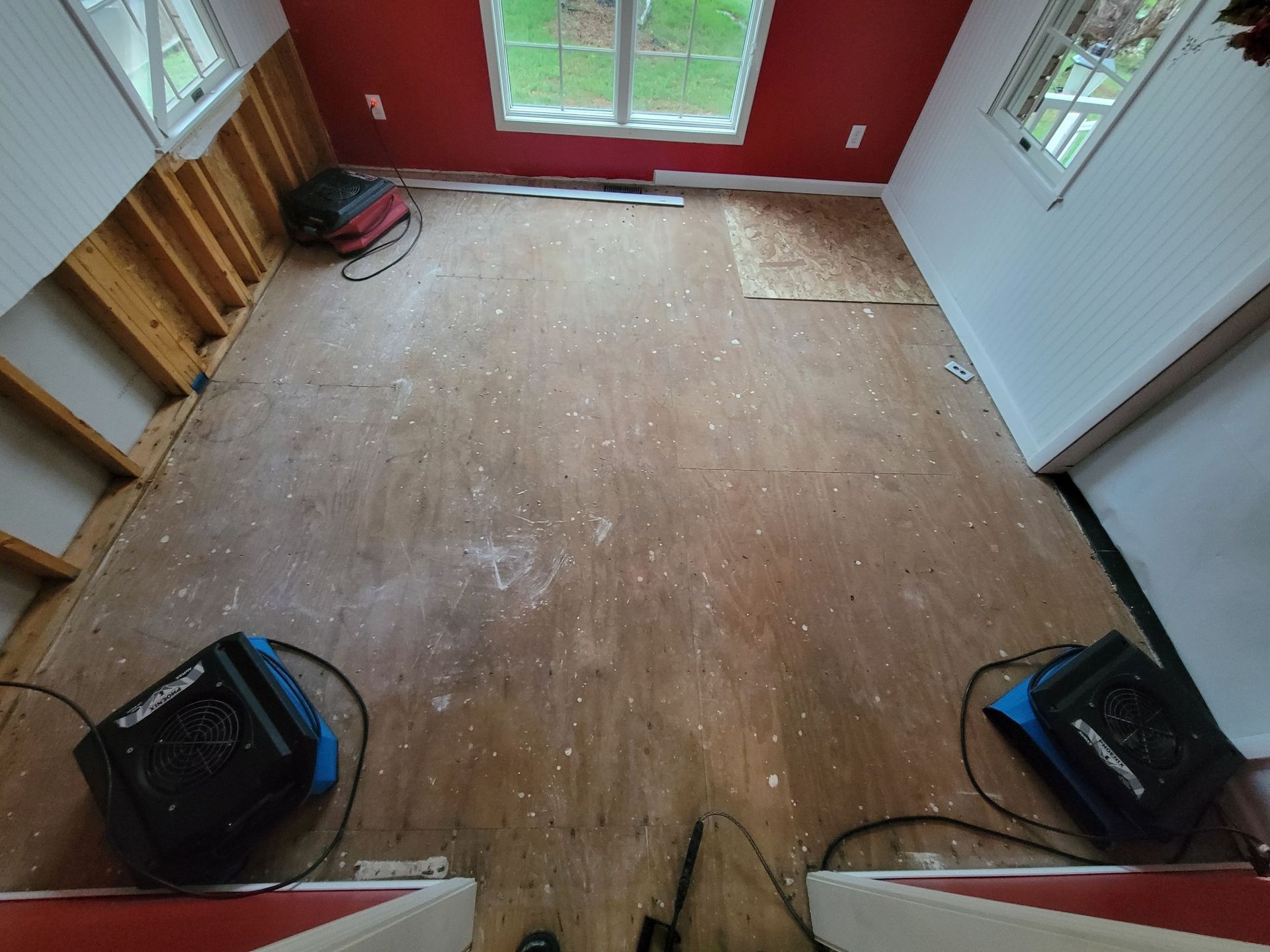 Room with exposed walls, drying equipment on the floor. Red and white walls with a window at the end.
