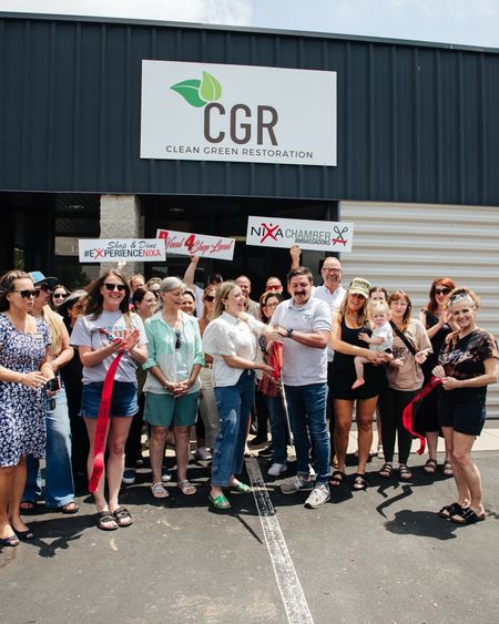 Ribbon-cutting ceremony outside the CGR facility. A group of people hold signs and smile.