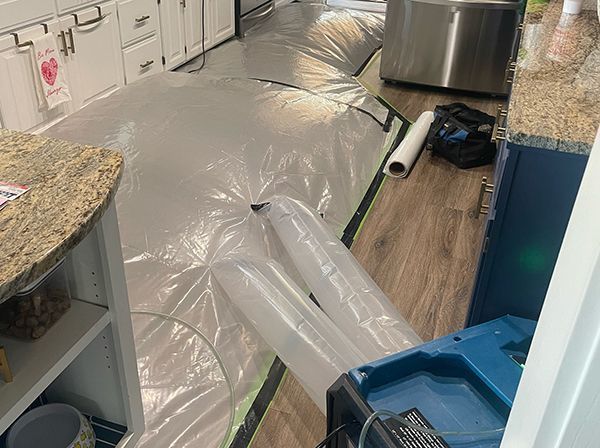 Kitchen with clear plastic sheeting and drying equipment on the floor, likely for water damage restoration.