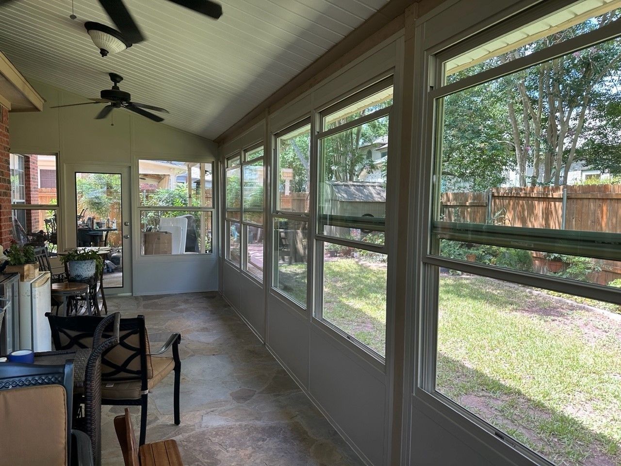 A screened in porch with a lot of windows and a ceiling fan.