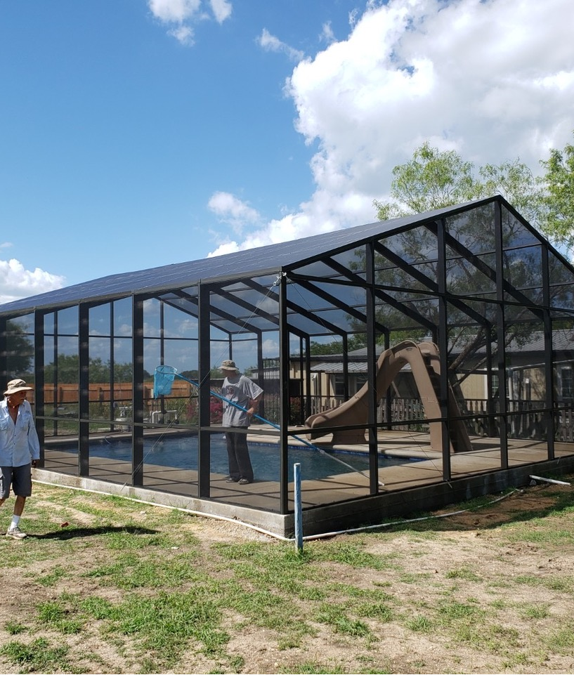 A man in a hat stands in front of a screened in swimming pool