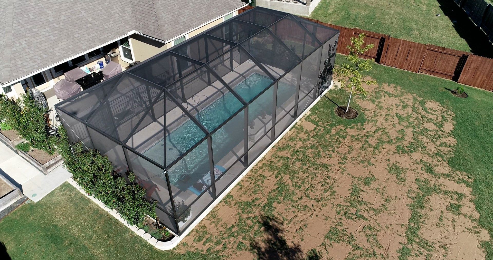 An aerial view of a screened in swimming pool in a backyard.