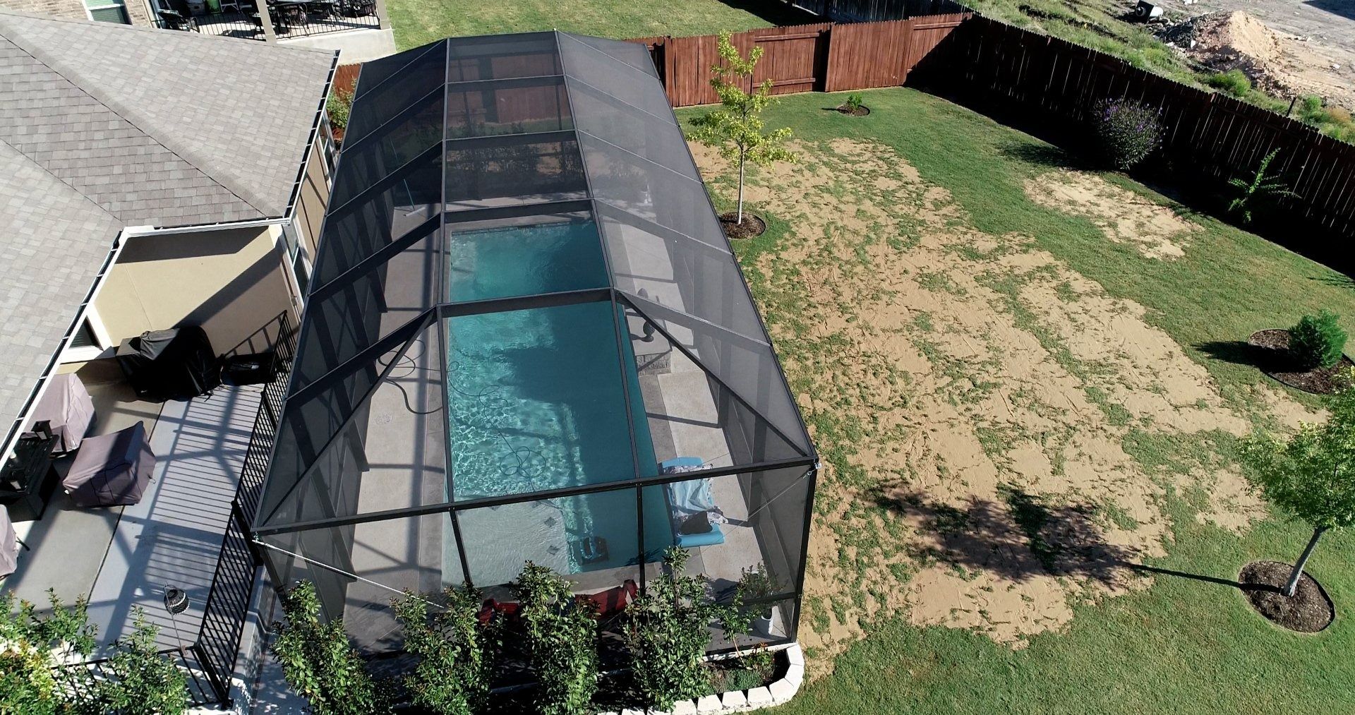 An aerial view of a screened in swimming pool in a backyard.