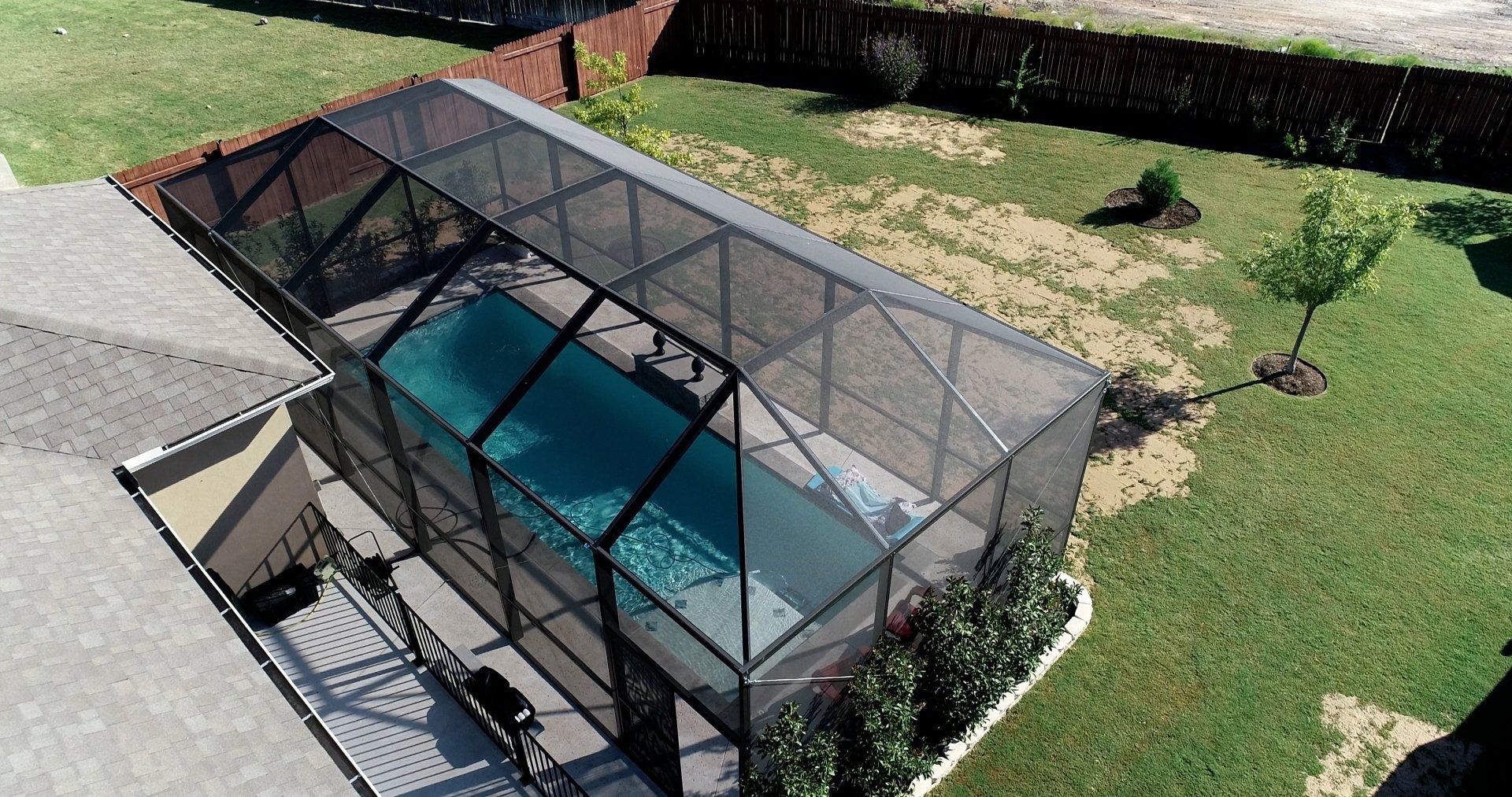 An aerial view of a screened in swimming pool in a backyard.