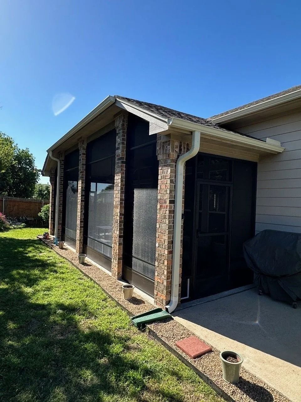 A house with a screened in porch and a grill in the backyard.