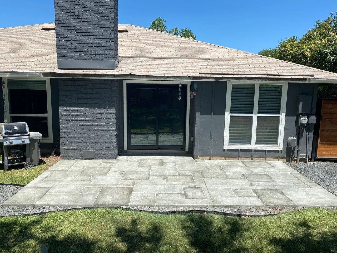 A house with a patio and a grill in front of it.