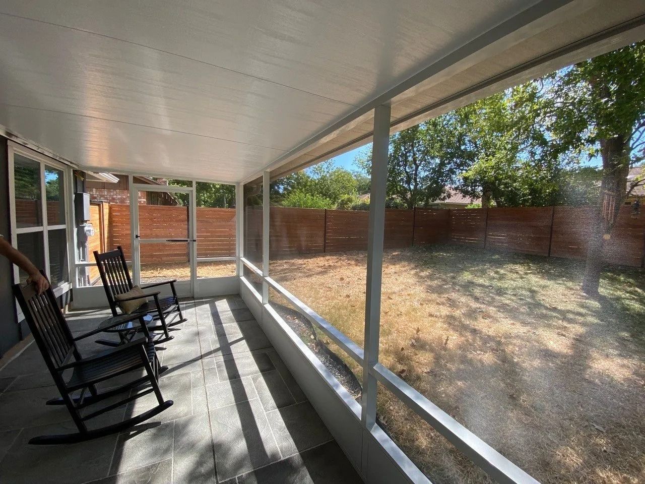 A screened in porch with rocking chairs and a view of the backyard.