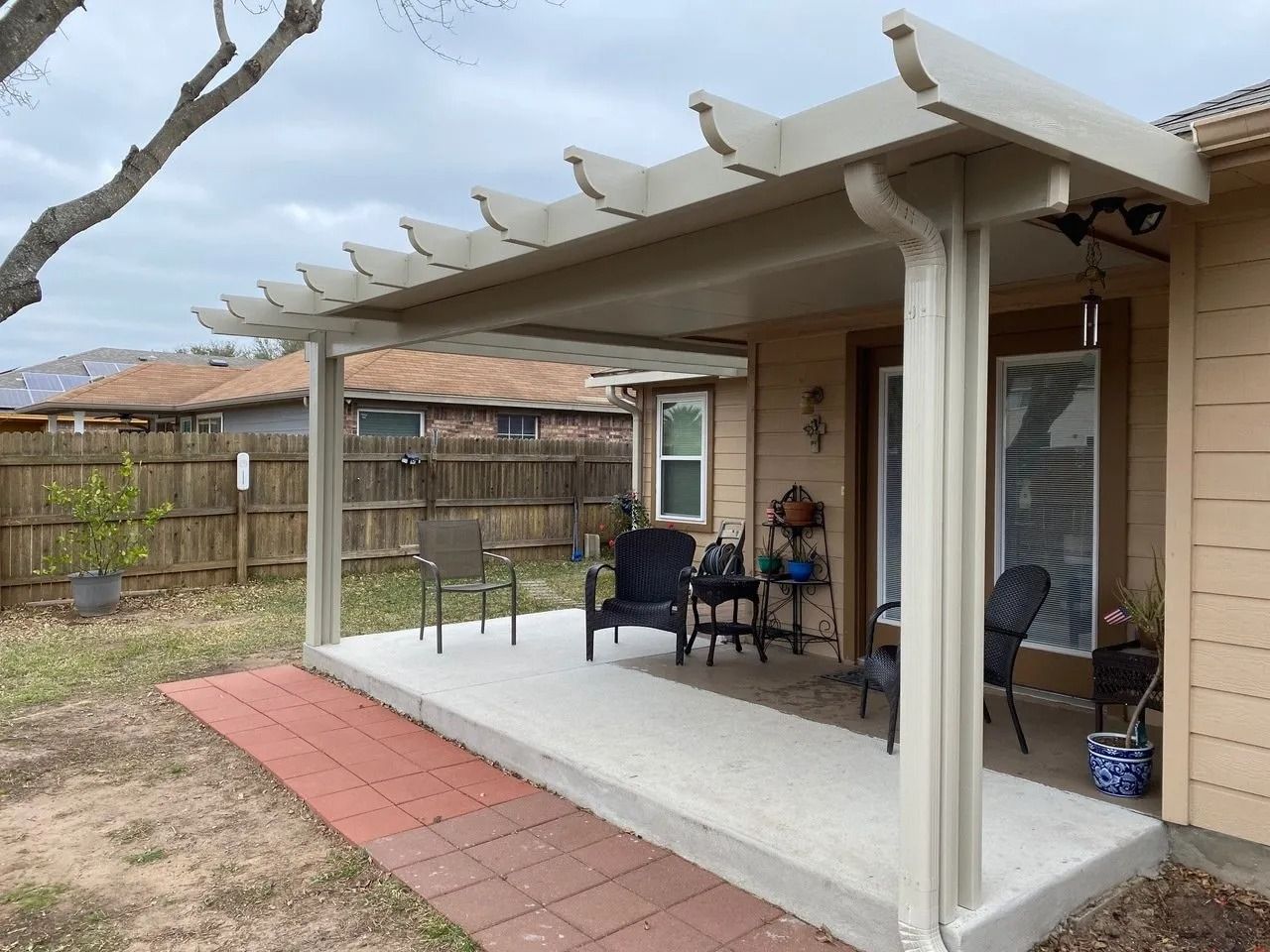 A patio with a pergola and chairs in the backyard of a house.