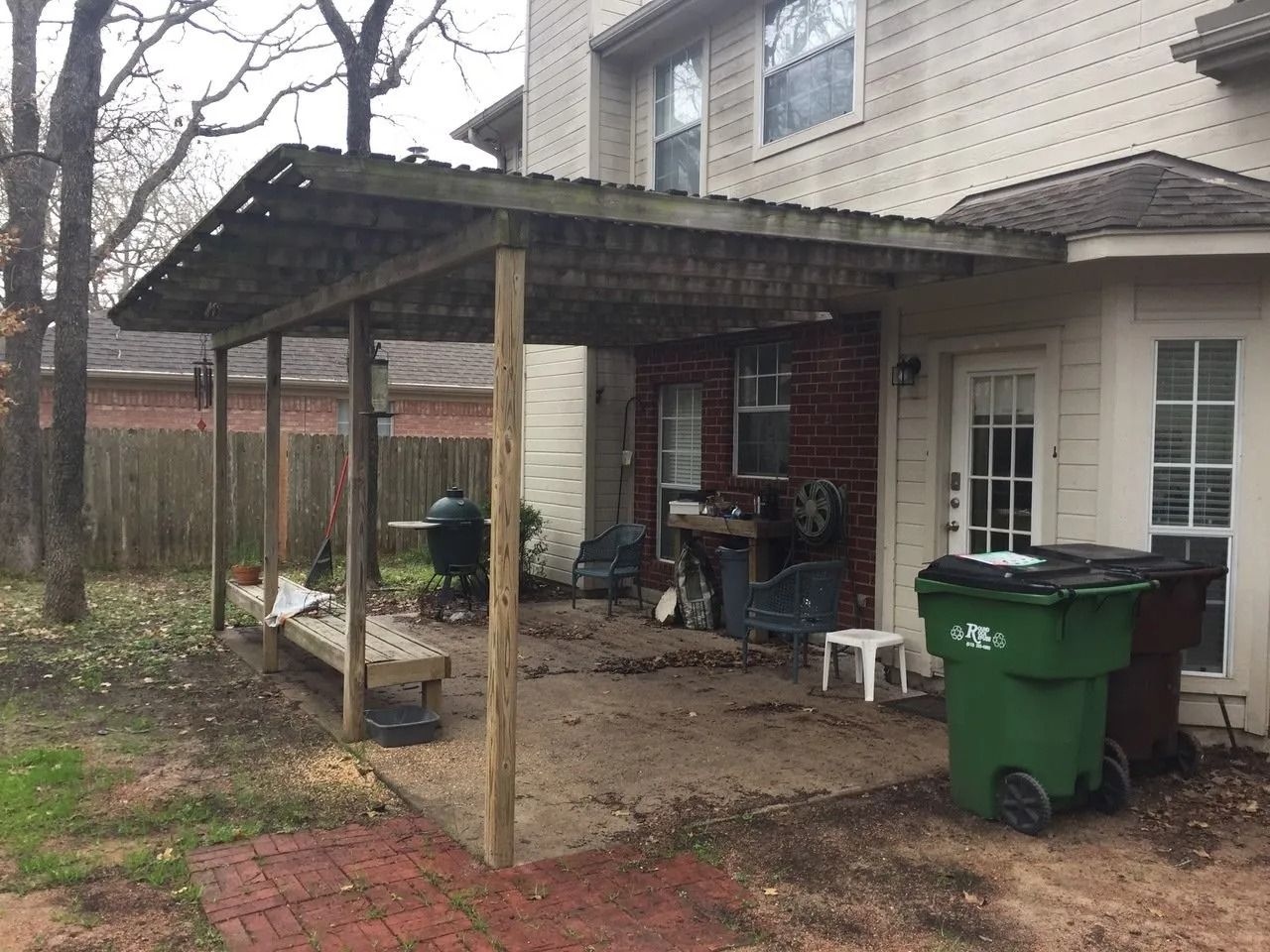 A covered patio with a trash can in front of a house.