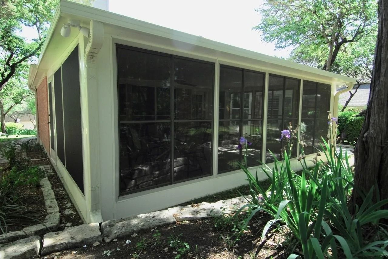 A screened in porch with a lot of windows and a tree in the background.