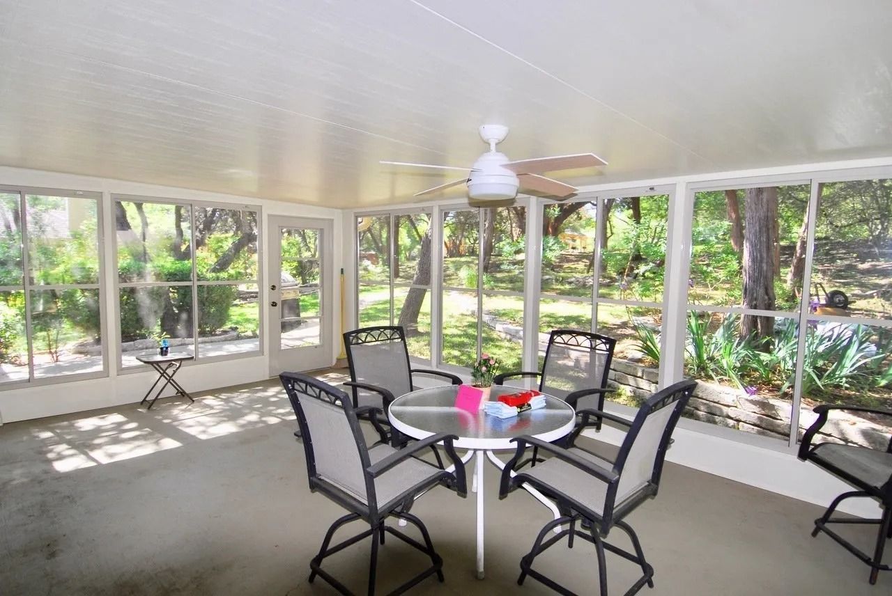 A screened in porch with a table and chairs and a ceiling fan.