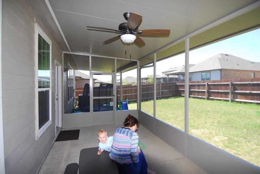 A woman is holding a baby in a screened in porch with a ceiling fan.