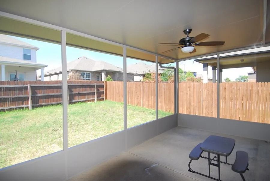 A screened in porch with a picnic table and a ceiling fan.
