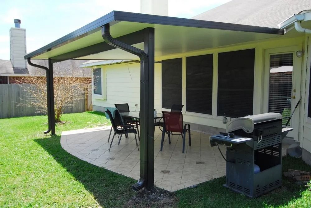 A covered patio with a table and chairs and a grill