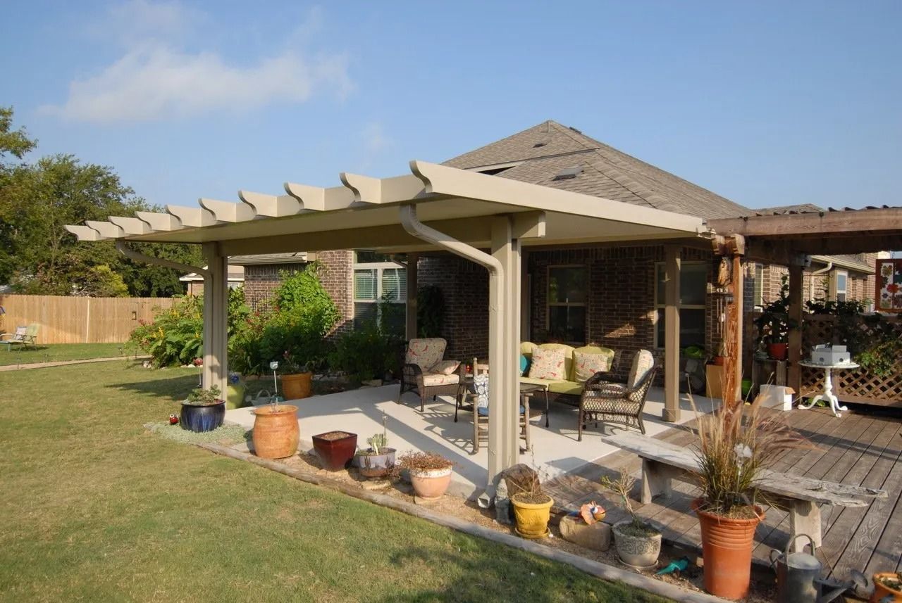 A patio with a pergola and potted plants in front of a house.