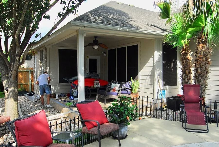 A man is standing on a porch with red chairs and a table