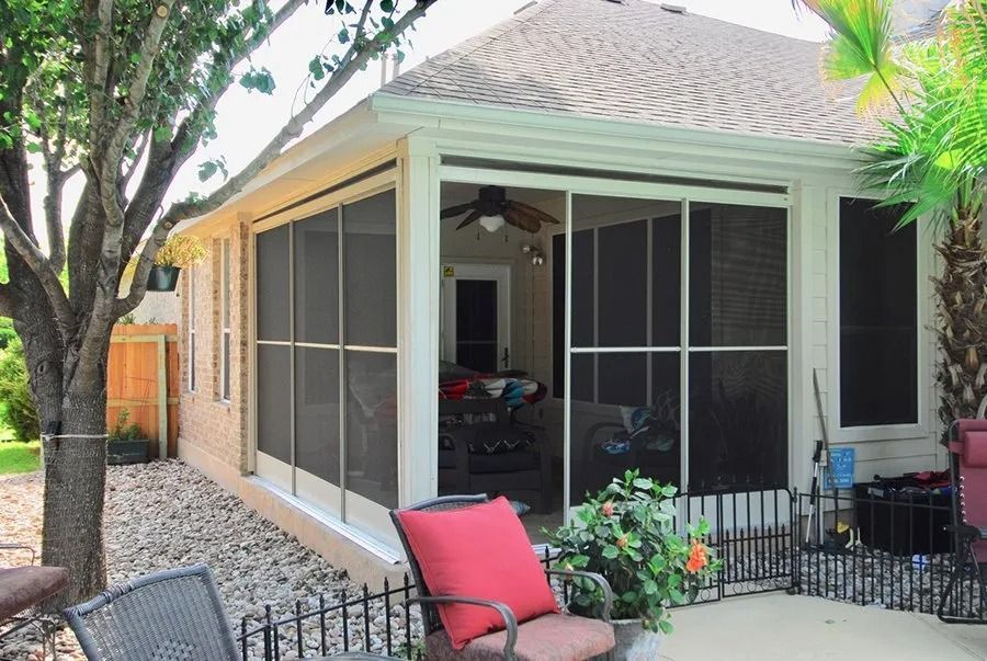 A screened in porch with chairs and a table in front of a house.