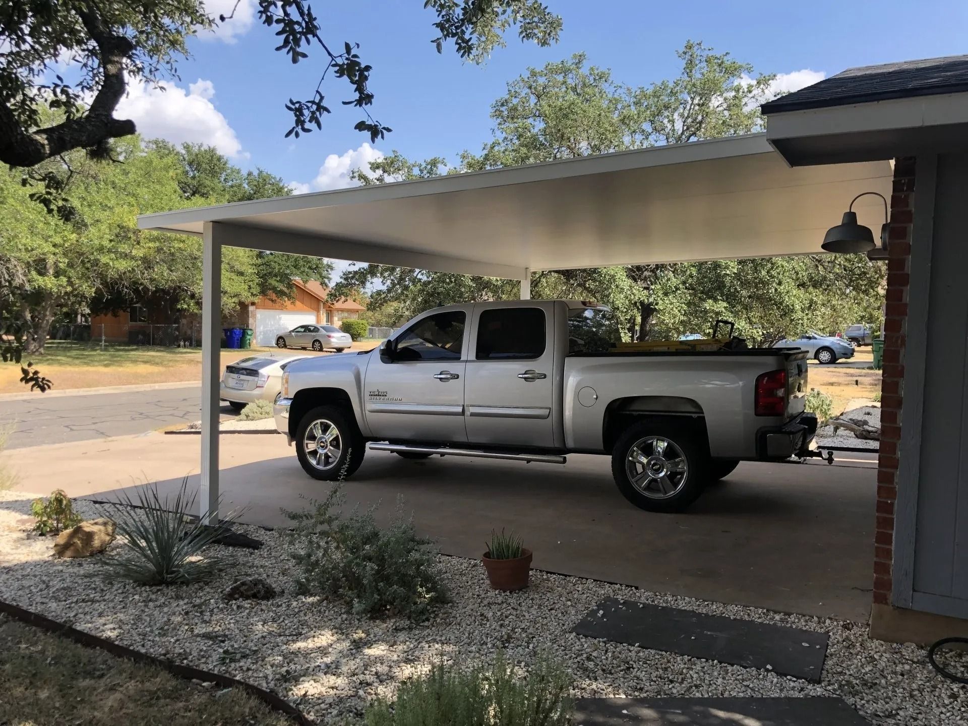 A silver truck is parked under a carport in front of a house.