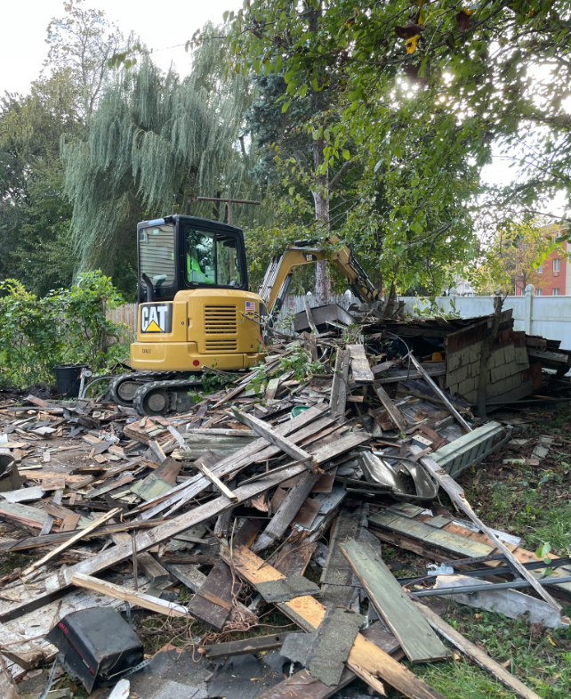 A cat excavator is sitting on top of a pile of wood.