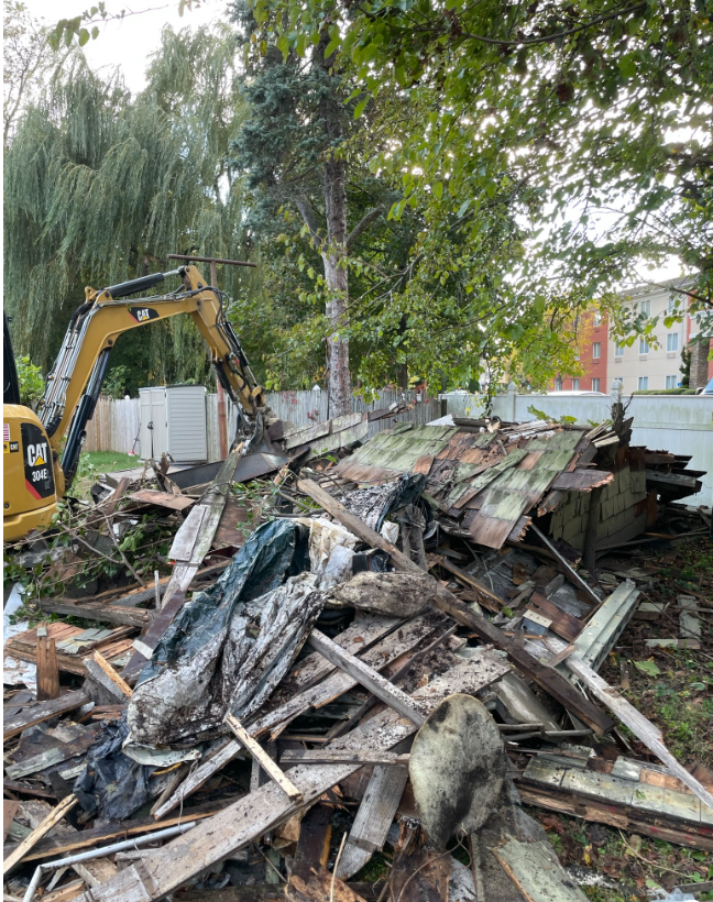 A pile of wood is being demolished by an excavator.